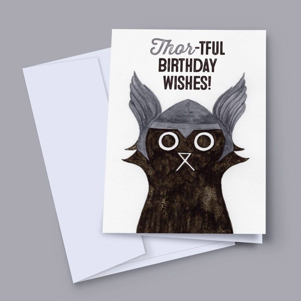 A 7x5 inch birthday card featuring an ink and salt black cat illustration wearing Thor's helmet