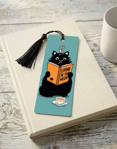 A bookmark featuring a black cartoon cat reading a book titled "Living in the Meow" with a mouse sitting on its head enjoying a cup of tea
